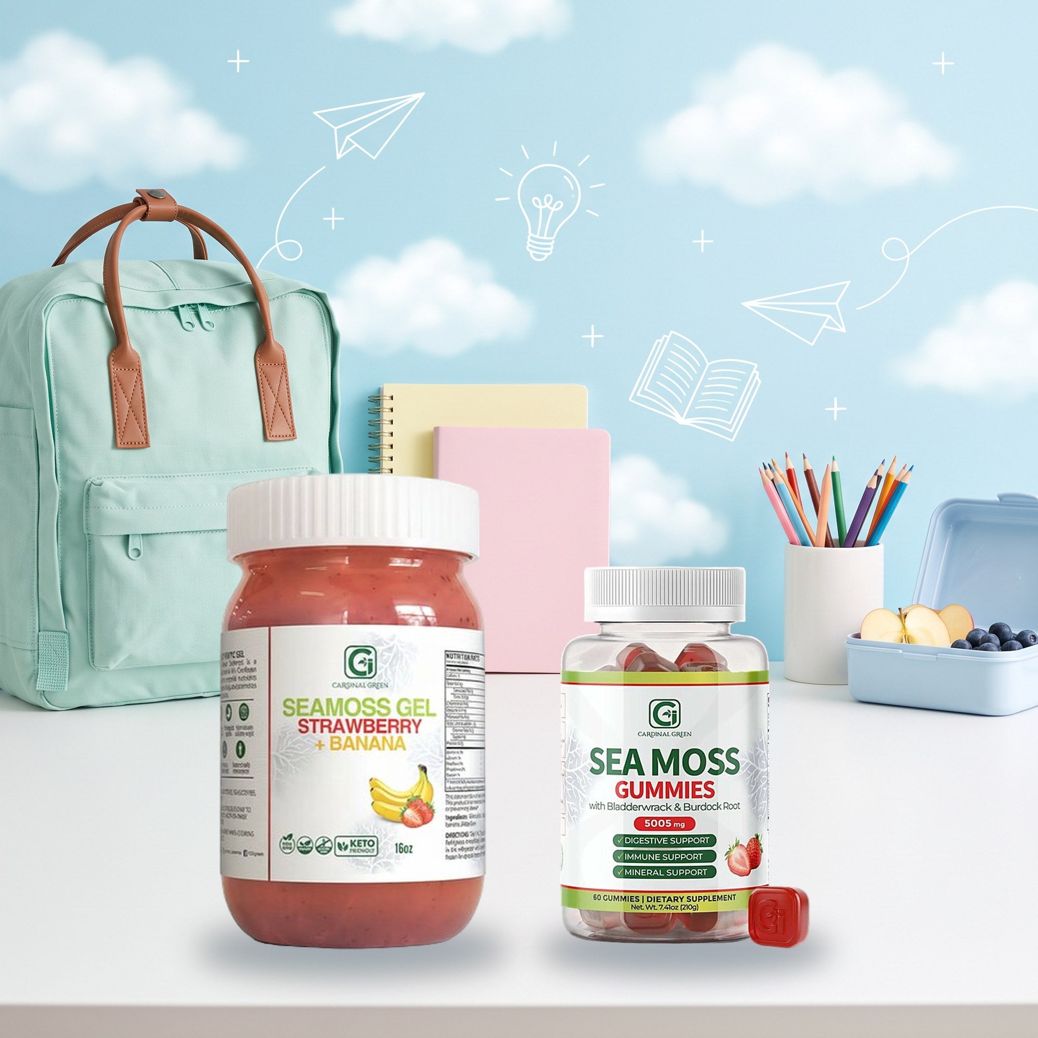 A 16 oz jar of CGI-Green Strawberry Banana fruit-infused sea moss gel and a bottle of CGI-Green Sea Moss Gummies on a desk beside a school backpack, notebooks, pencils and a packed lunchbox