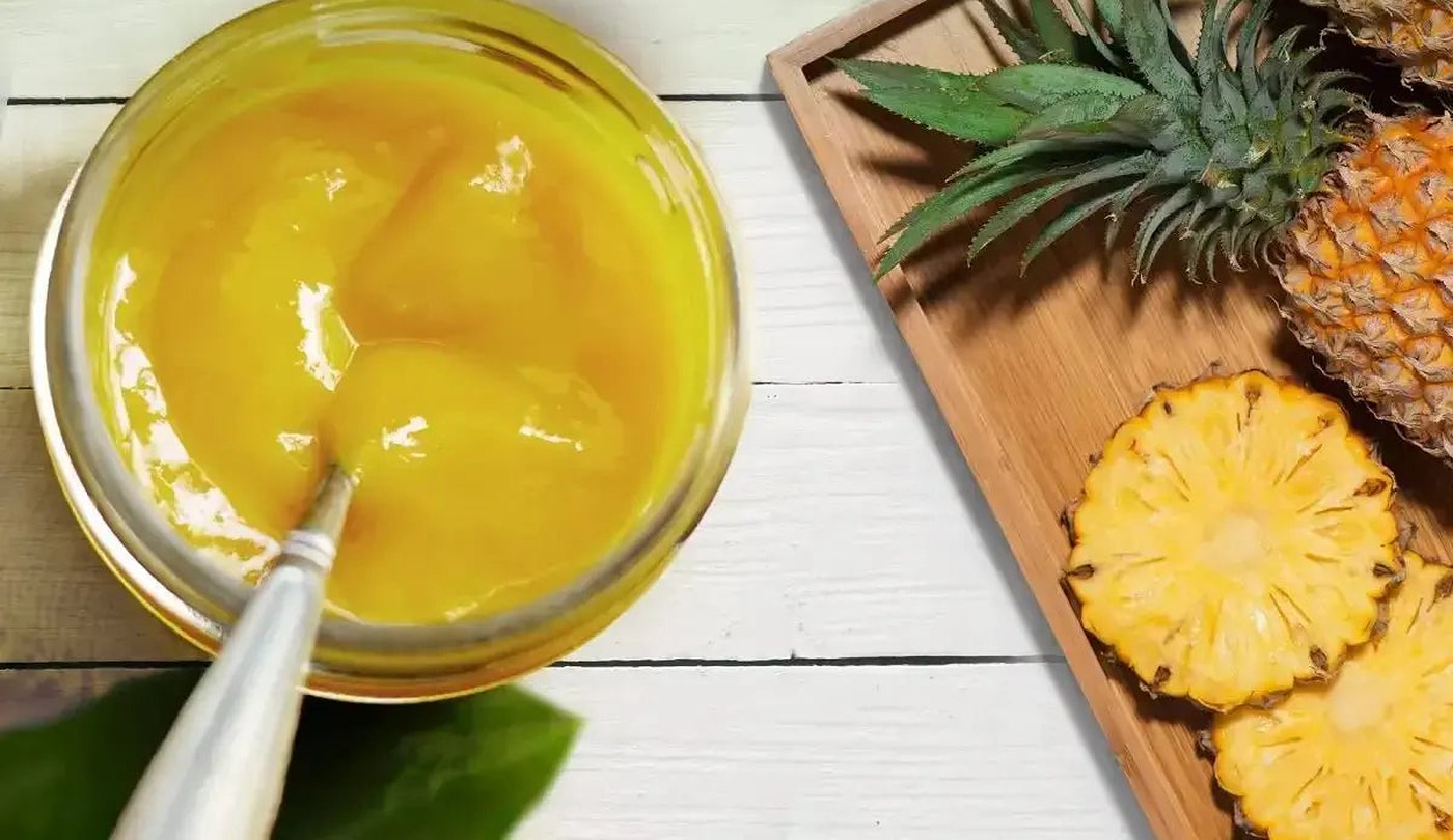 Spoon lifting smooth golden pineapple sea moss gel from a glass bowl beside sliced pineapple
